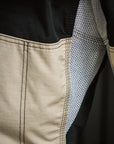 Close-up detail of a garment showing a beige fabric panel with black double-stitched seams, a black interior lining, and a textured gray-and-white mesh inner layer.